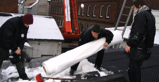Ein verschneites Firmendach und drei Arbeiter